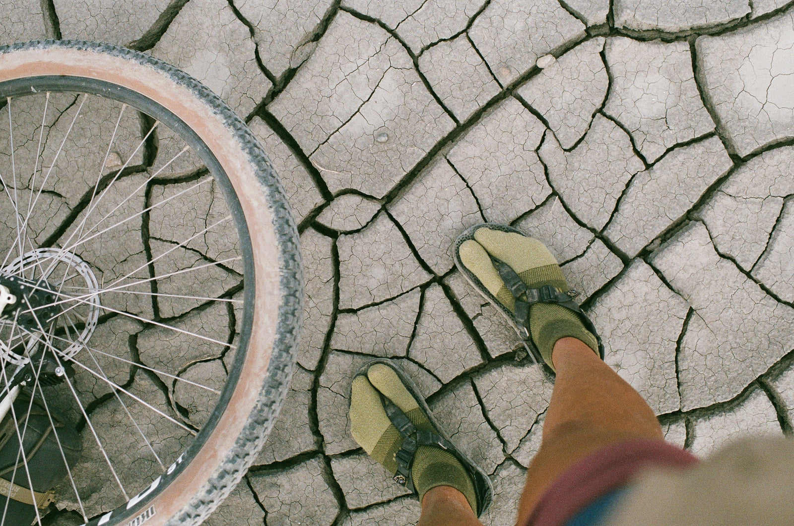 person looking down at feet standing on mud cracks wearing bedrock sandals