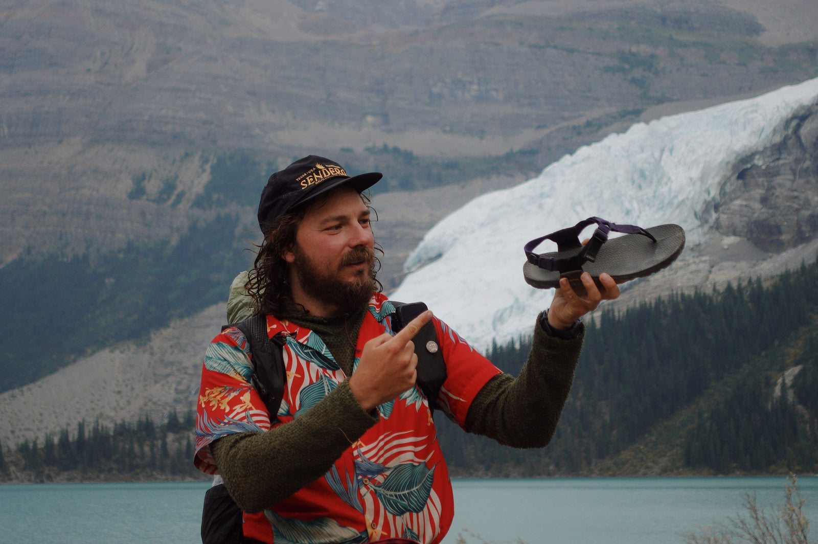 Jarhead stands in front of a mountain and looks at this sandal in hand, pointing to it.