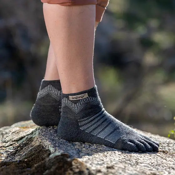 A person wearing a pair of Injinji Merino wool midweight mini-crew socks in gray color with toe separation on a rock outside.