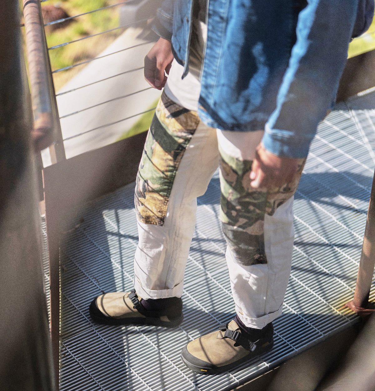 A person wearing camo patterned pants and Driftwood gray Nubuck leather Mountain Clogs in an urban setting