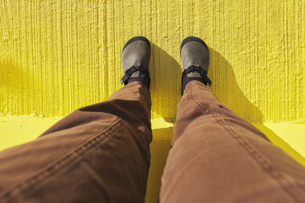 person wearing gray nubuck leather mountain clogs POV on a yellow pavement