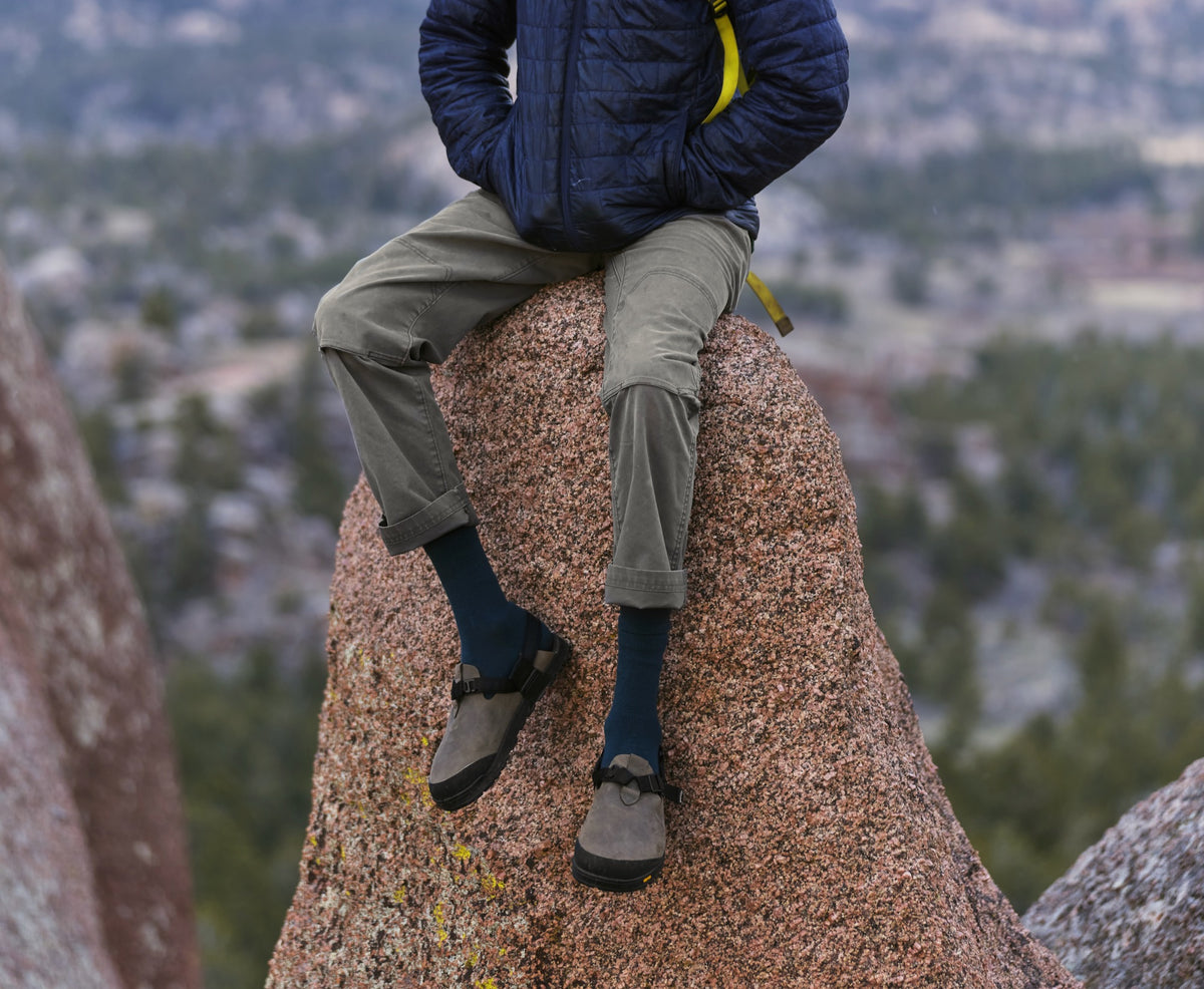 A person sitting on a granite boulder wearing Driftwood gray Nubuck leather Mountain Clogs