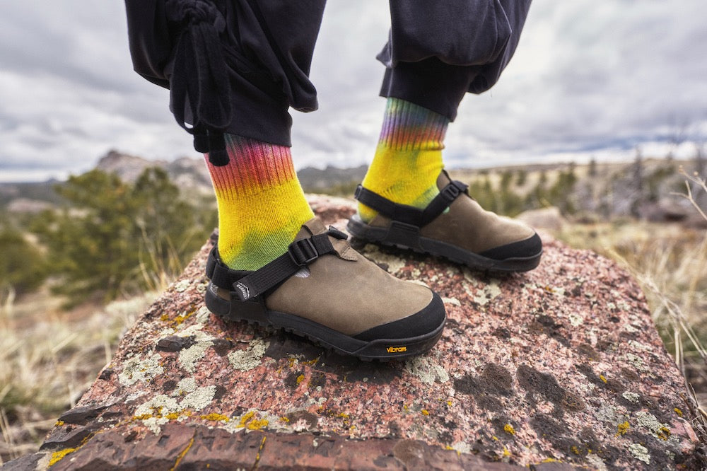 person wearing rainbow colored socks and gray nubuck leather clogs