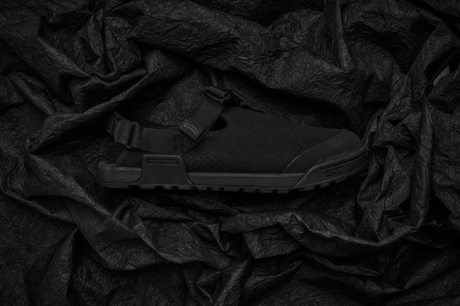 studio photo of black synthetic suede clogs on crumpled black fabric background