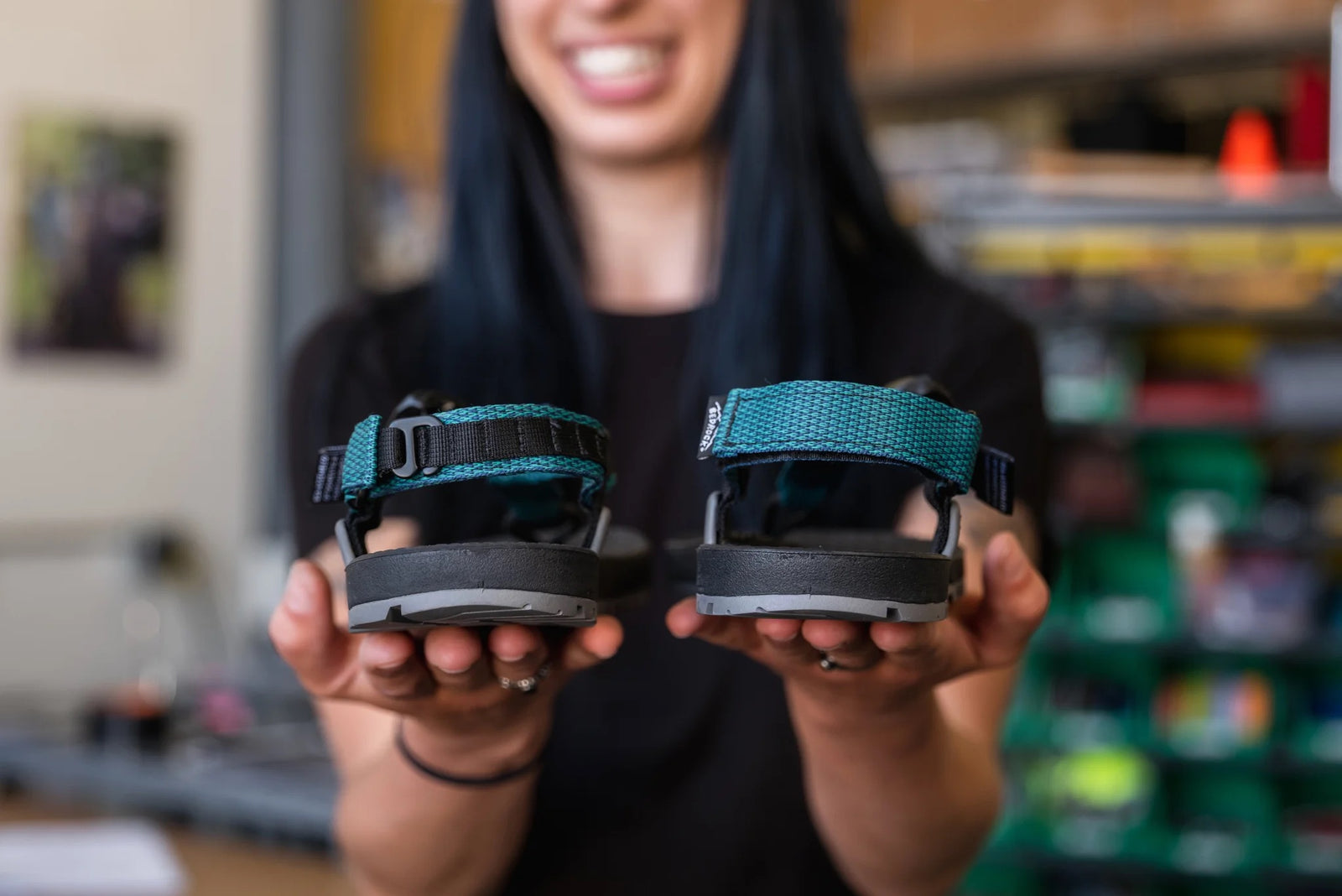 Person holding sandals with teal straps showing both heel hook-and-loop and velcro heel closures