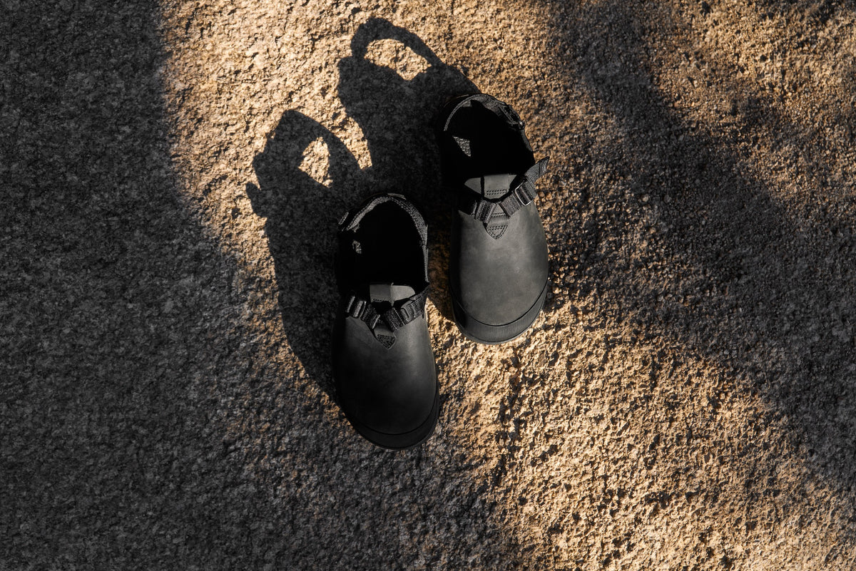 Pair of Obsidian Dark Gray Mountain Clogs on a textured surface with a soft focus