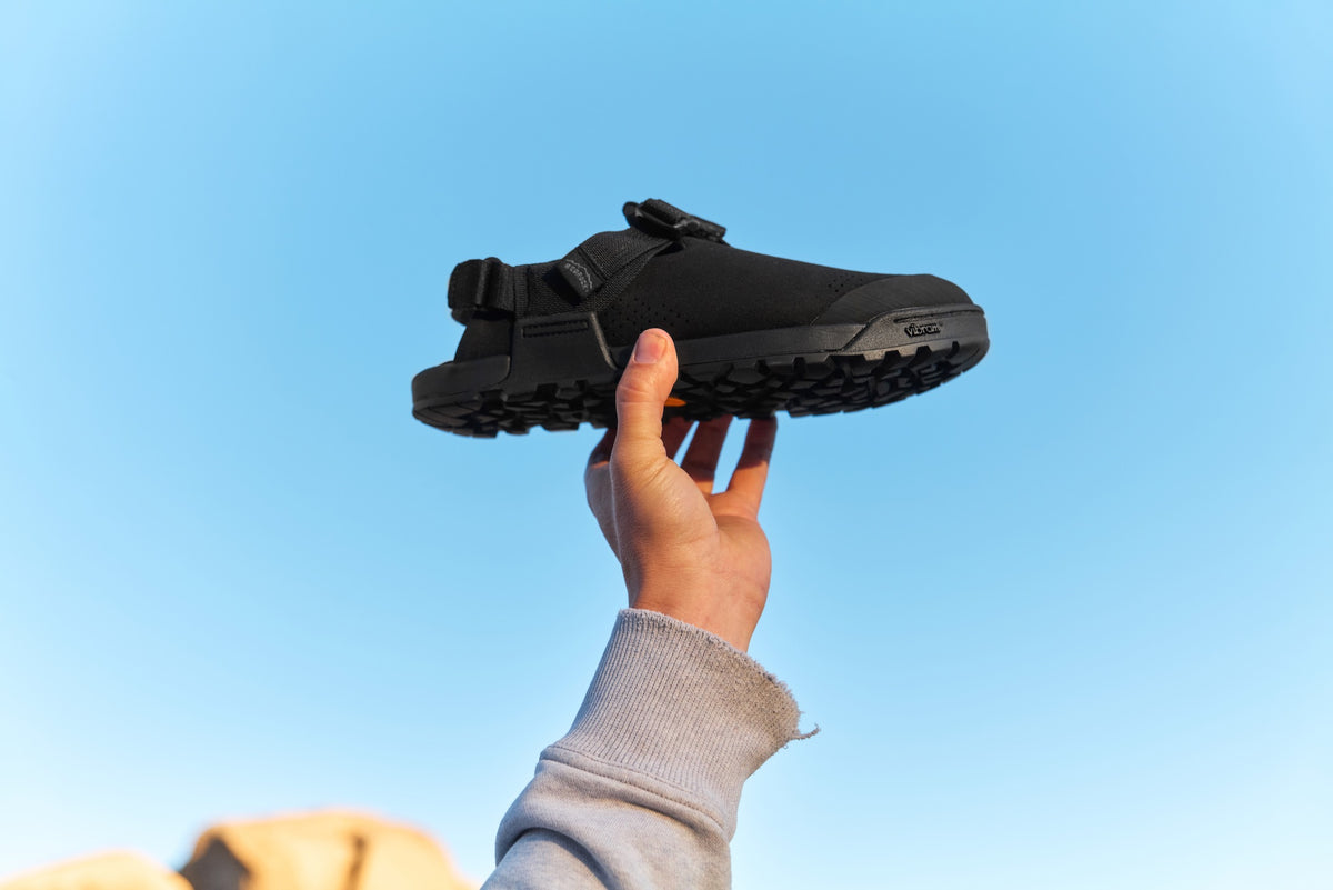 Person holding Obsidian Black Synthetic Mountain Clogs Heel against a clear blue sky