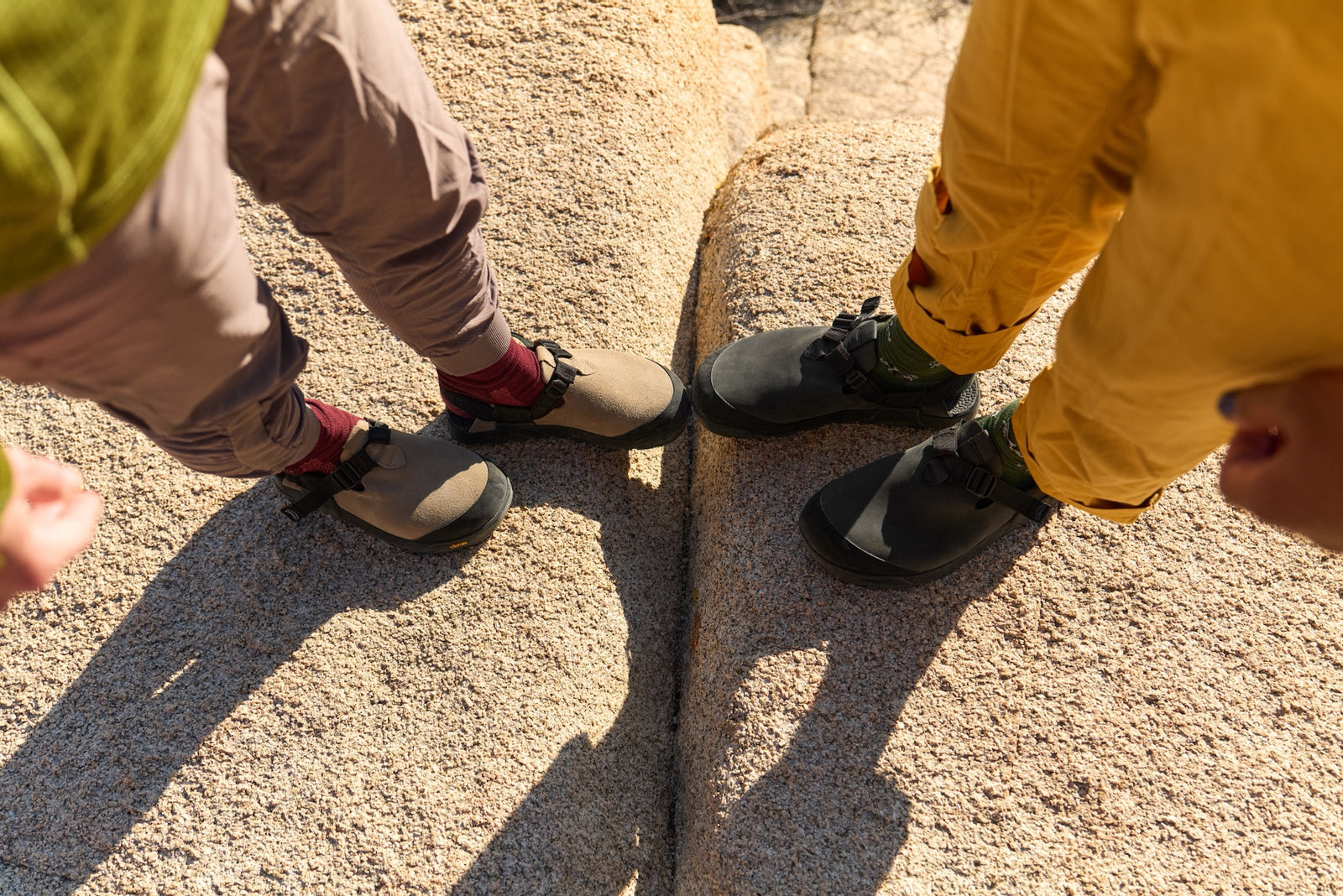 Two people wearing mountaion clogs on a rocky surface