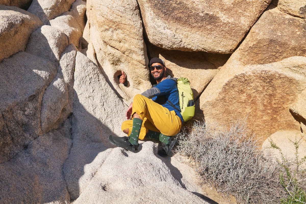 Person in outdoor gear sitting among large rocks with a backpack wearing Obsidian Dark Gray Mountain Clogs