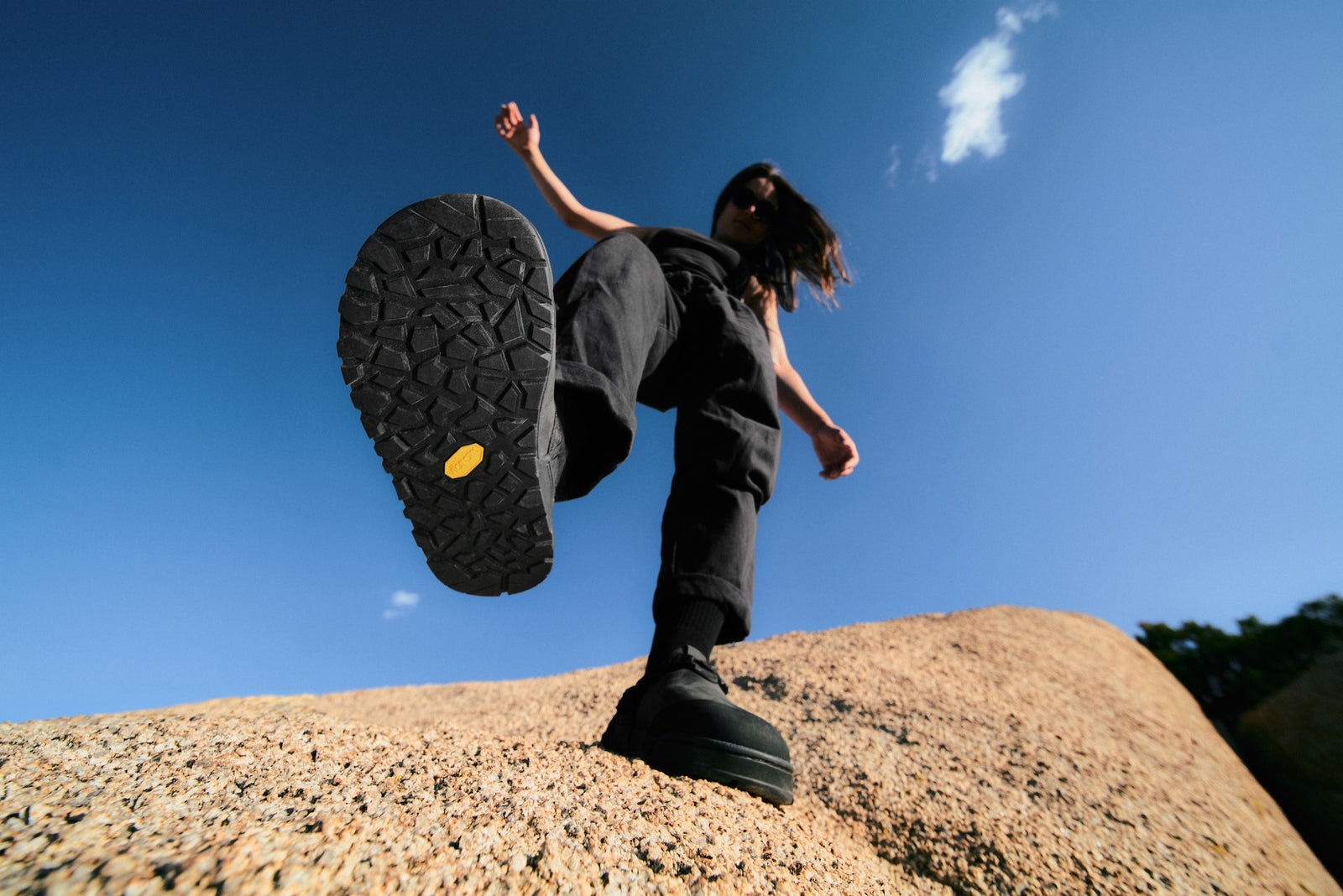 Person wearing obsidian dark gray nubuck leather mountain clogs against a blue sky.