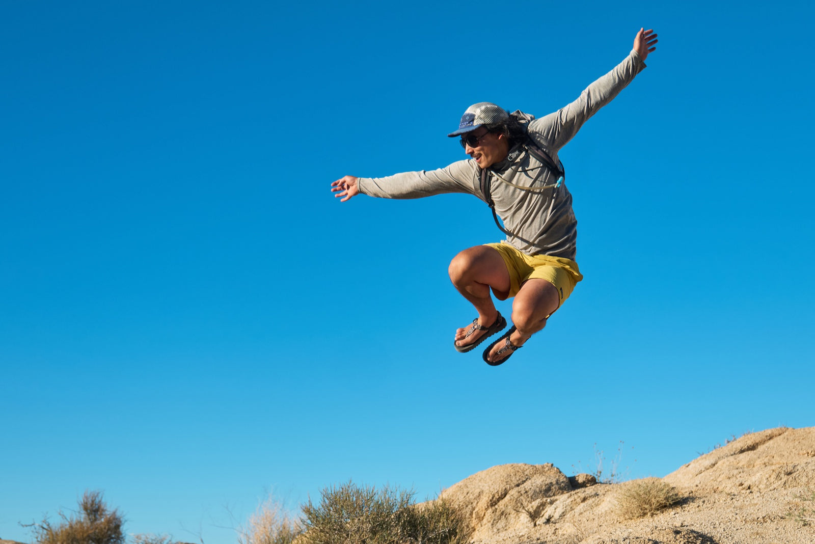 Person jumping in the air with a clear blue sky and desert landscape wearing Bedrock Cairn Sandals