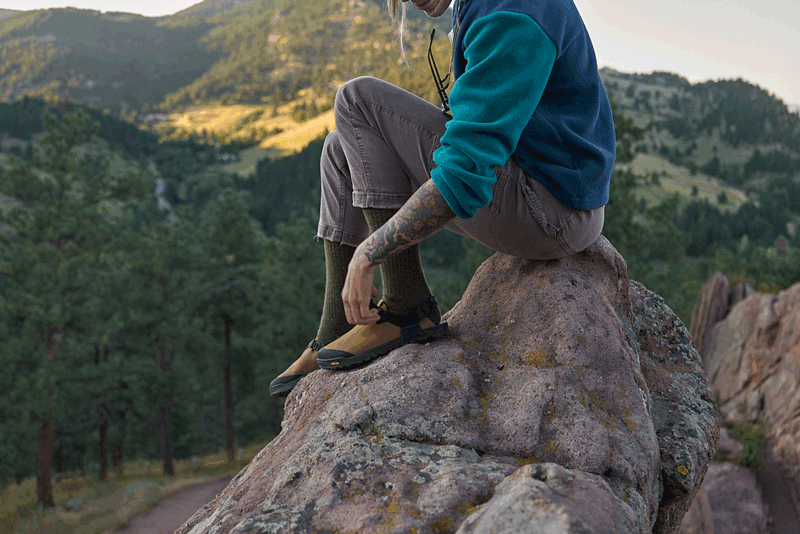 person adjusting brown nubuck leather mountain clogs on a rock