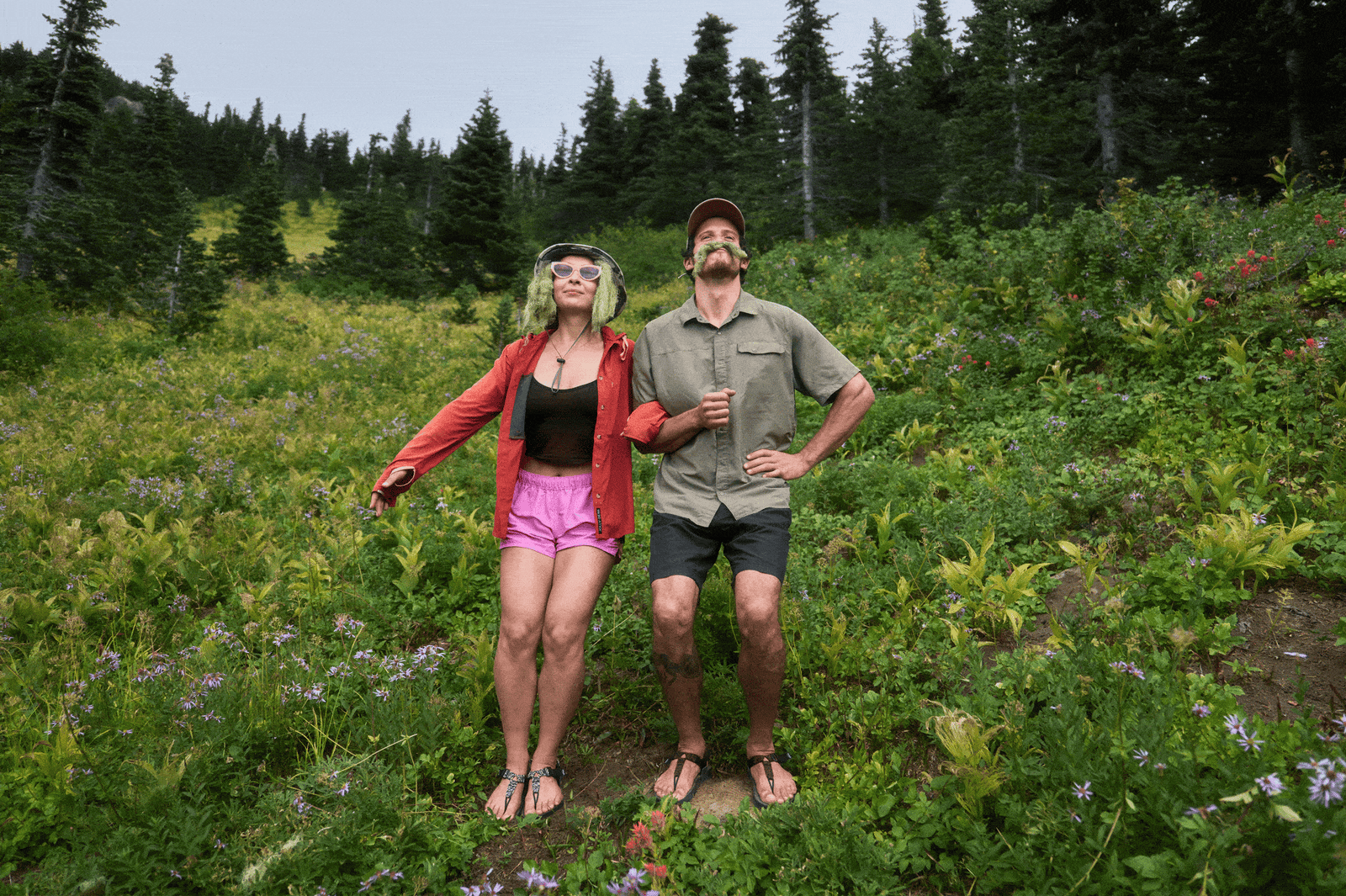 Two People jumping up and down along a green grassy slope wearing Cairn Evo C PRO sandals