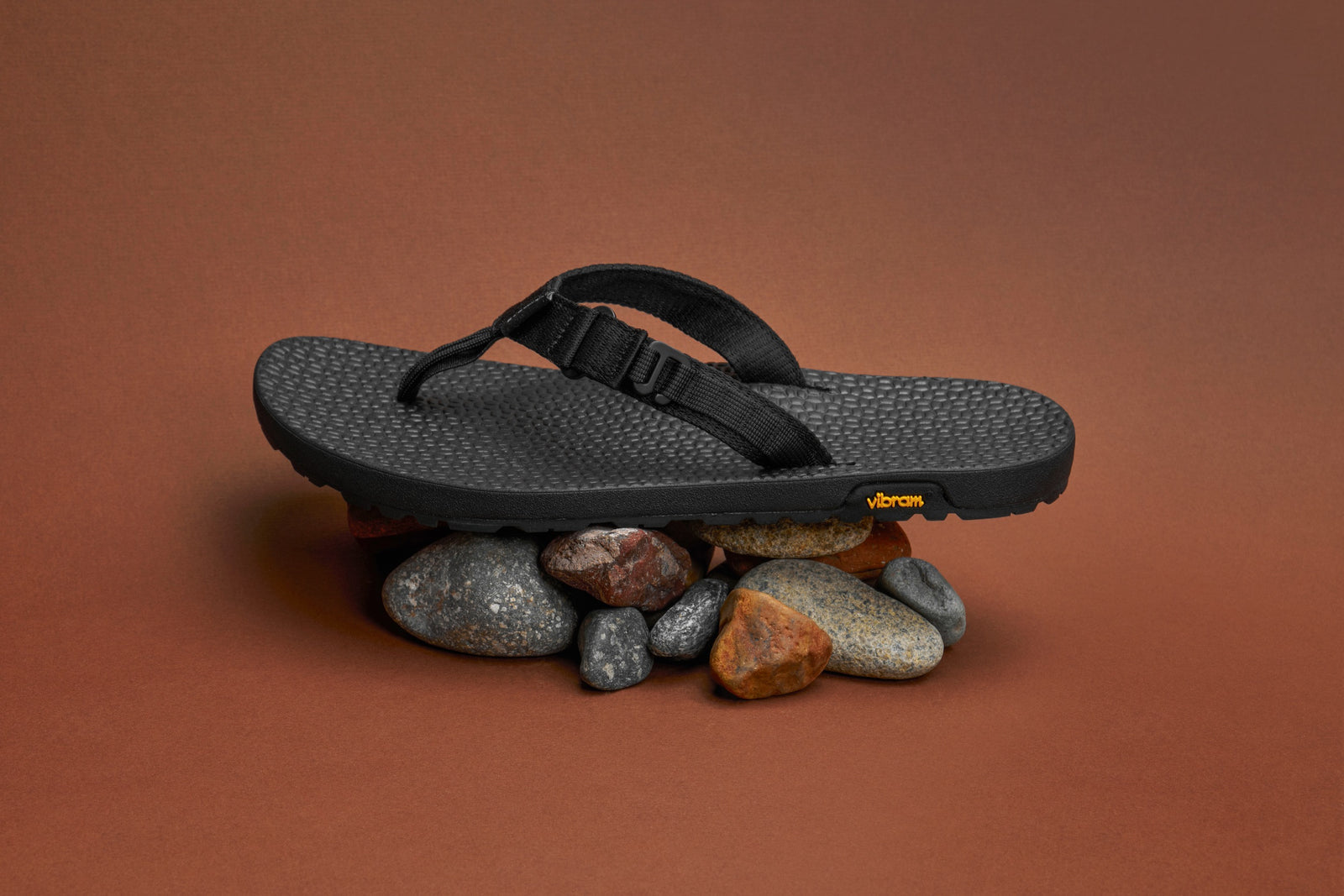 Black Rockhound sandal with a strap on rocks against a brown background