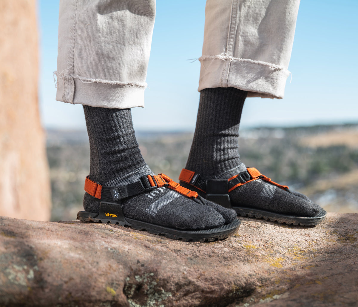 A person wearing a pair of cairn sandals with a pair of gray Bedrock x Injinji crew split-toe socks on.