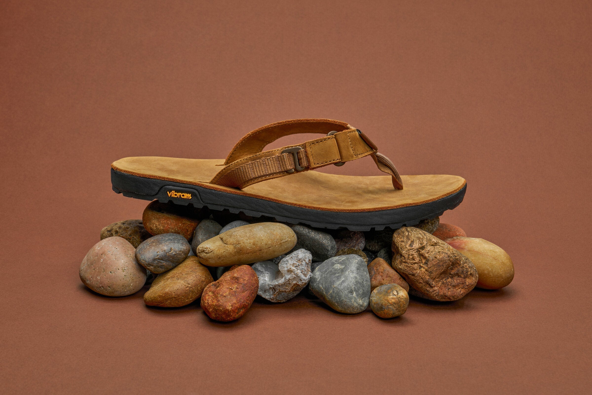 leather rockhound sandals sitting on stones with a brown backdrop