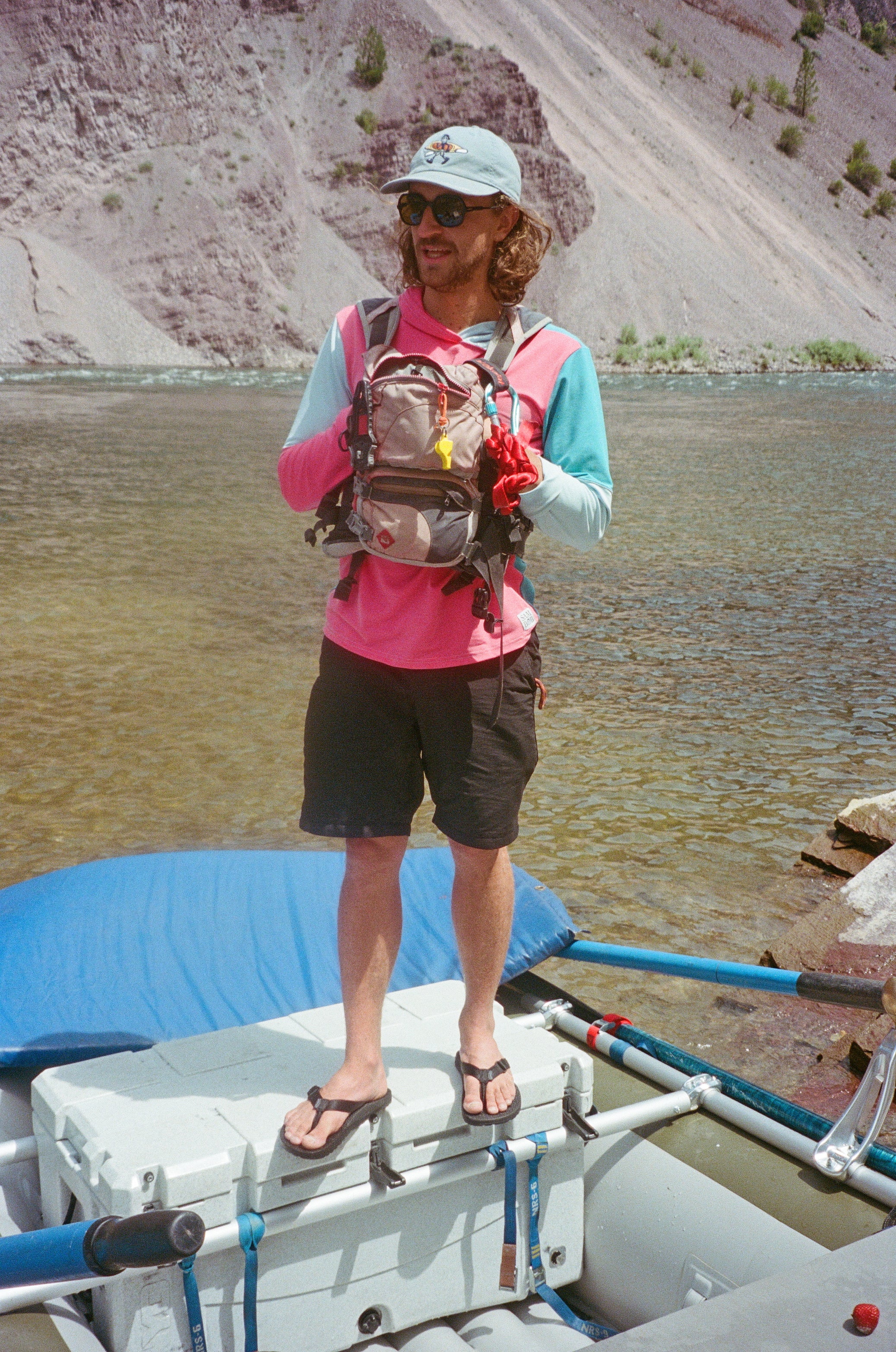 Person standing on a boat with a backpack near a body of water wearing black rockhound flip flops.