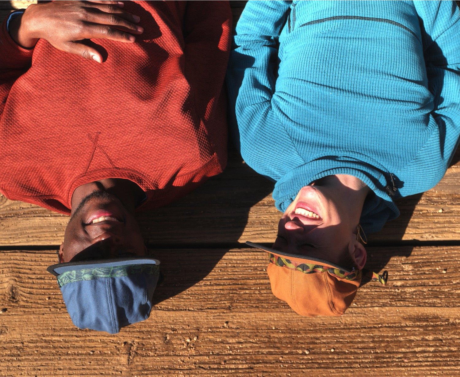 Two people laying on a wooden bridge wearing  blue and brown colored organic cotton canvas fabric hat webbing by KAVU and Bedrock.