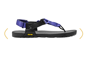 A Vibram sandal with a black footbed and sole, featuring purple straps, shown in a side profile on a white background with yellow curved arrows indicating width.