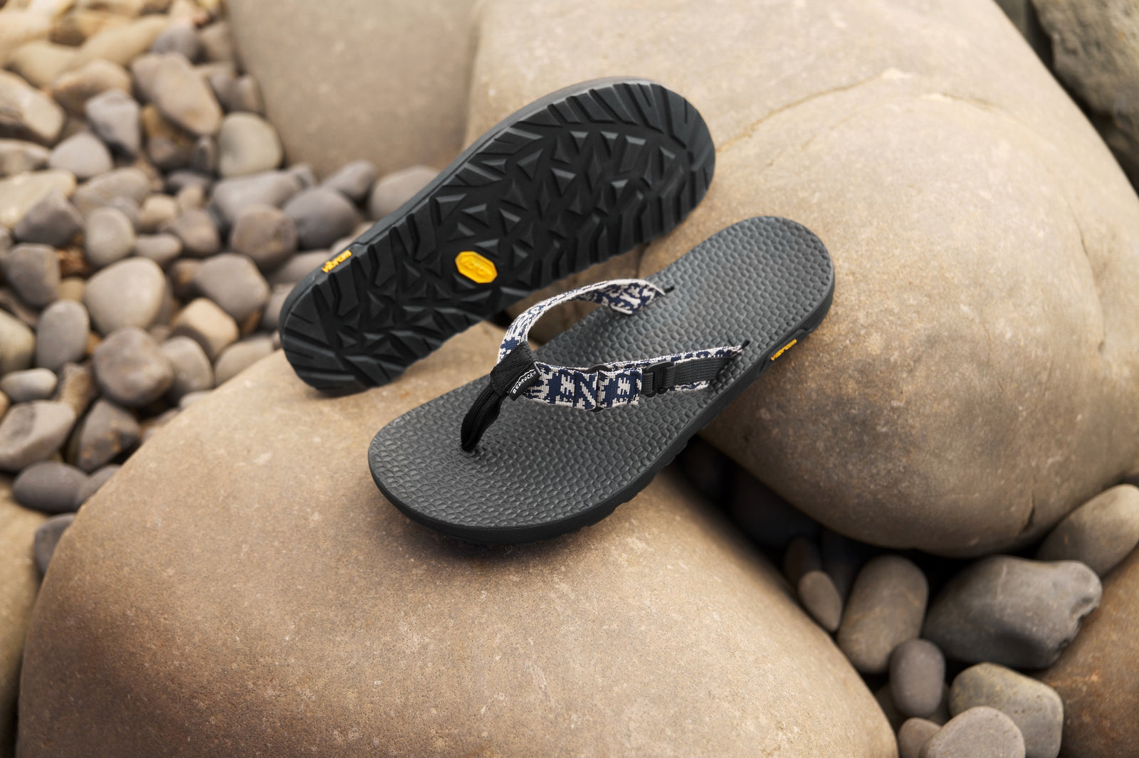 Abstract Navy Rockhound sandals sitting on a stone surface with pebbles in the background