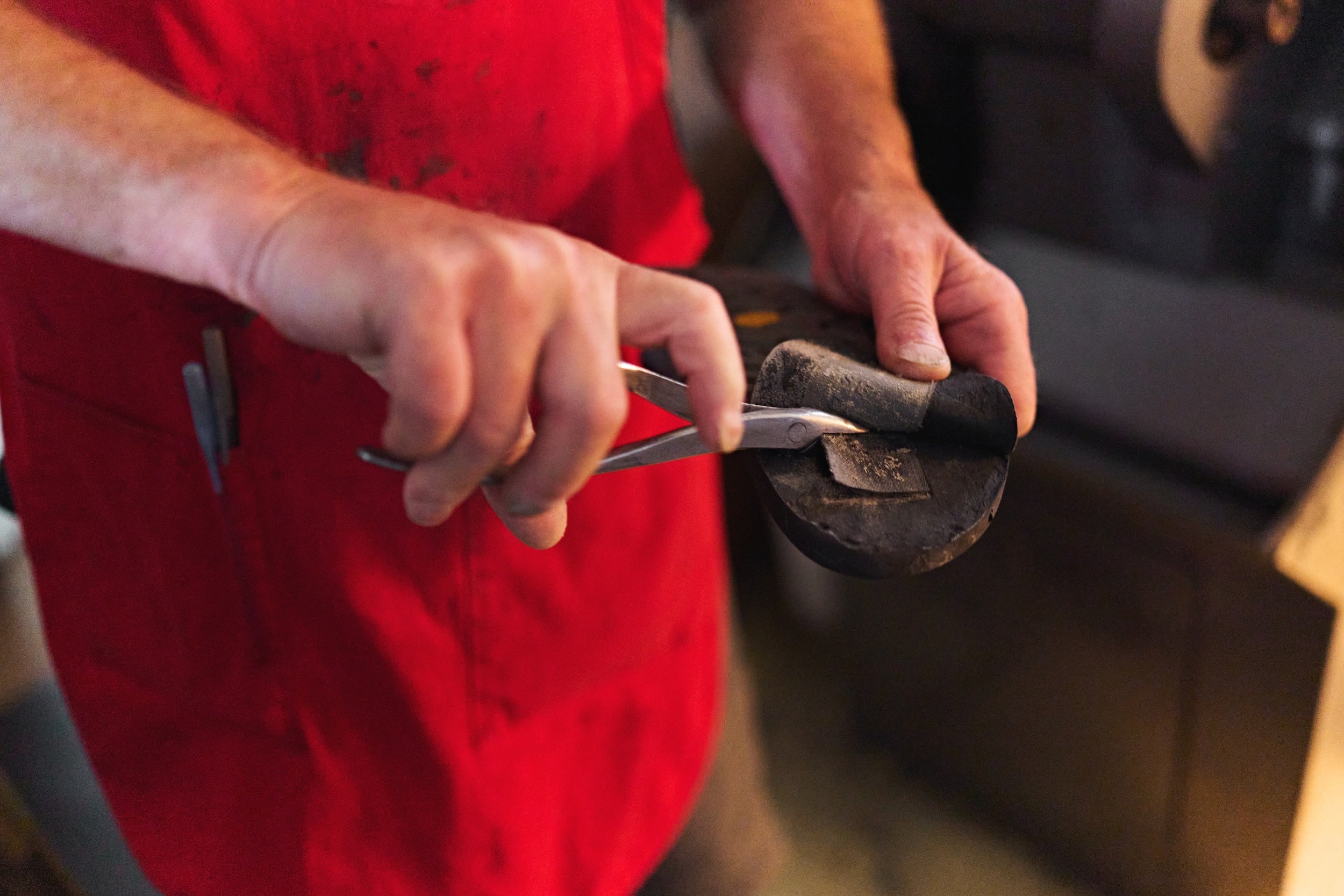Person in a red apron using a tool to remove a damaged toe post strap from a sandal