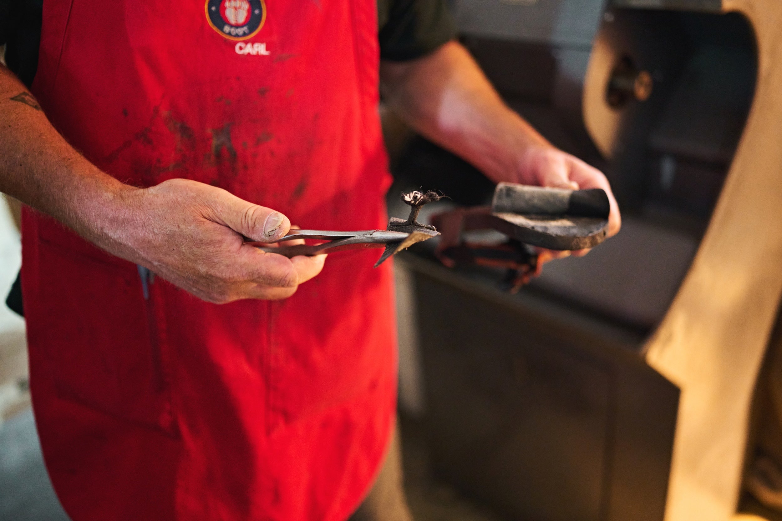 Person in a red apron holding a tool having removed a damaged toe post strap from a sandal
