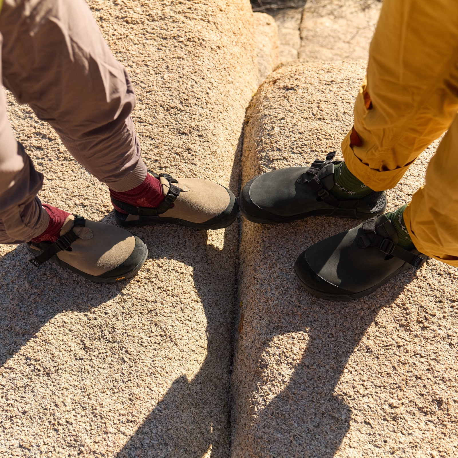 Two people wearing mountaion clogs on a rocky surface