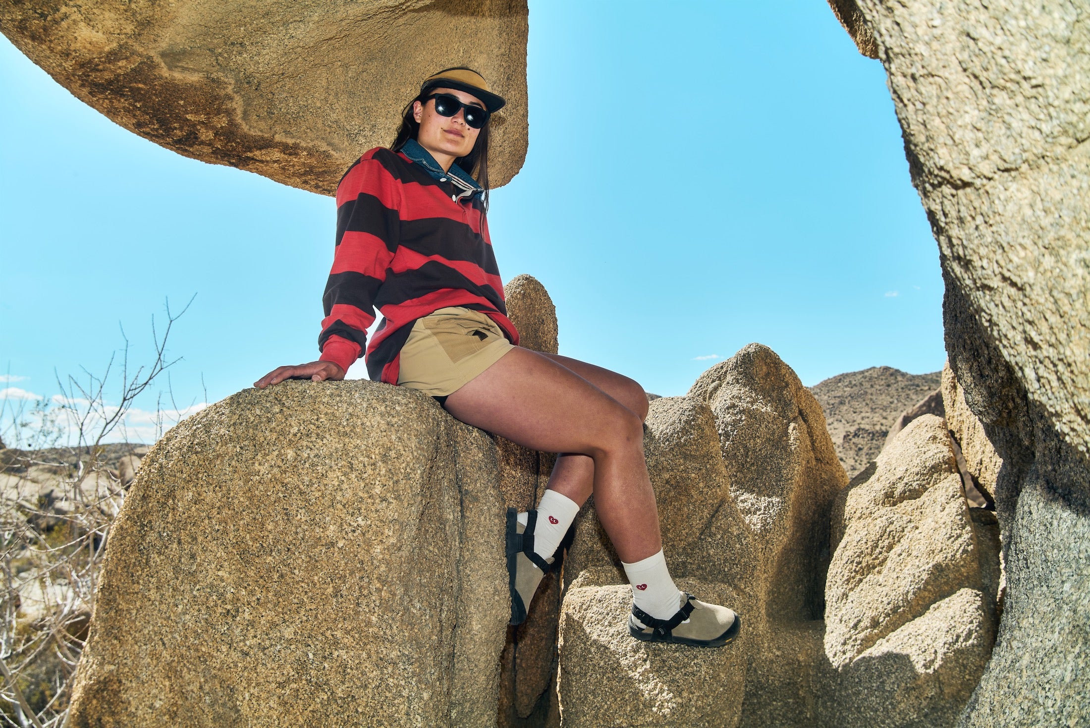 Person sitting on a rock in a desert landscape wearing a red and black striped shirt and Birch Bark Leather Suede Mountain Clogs 