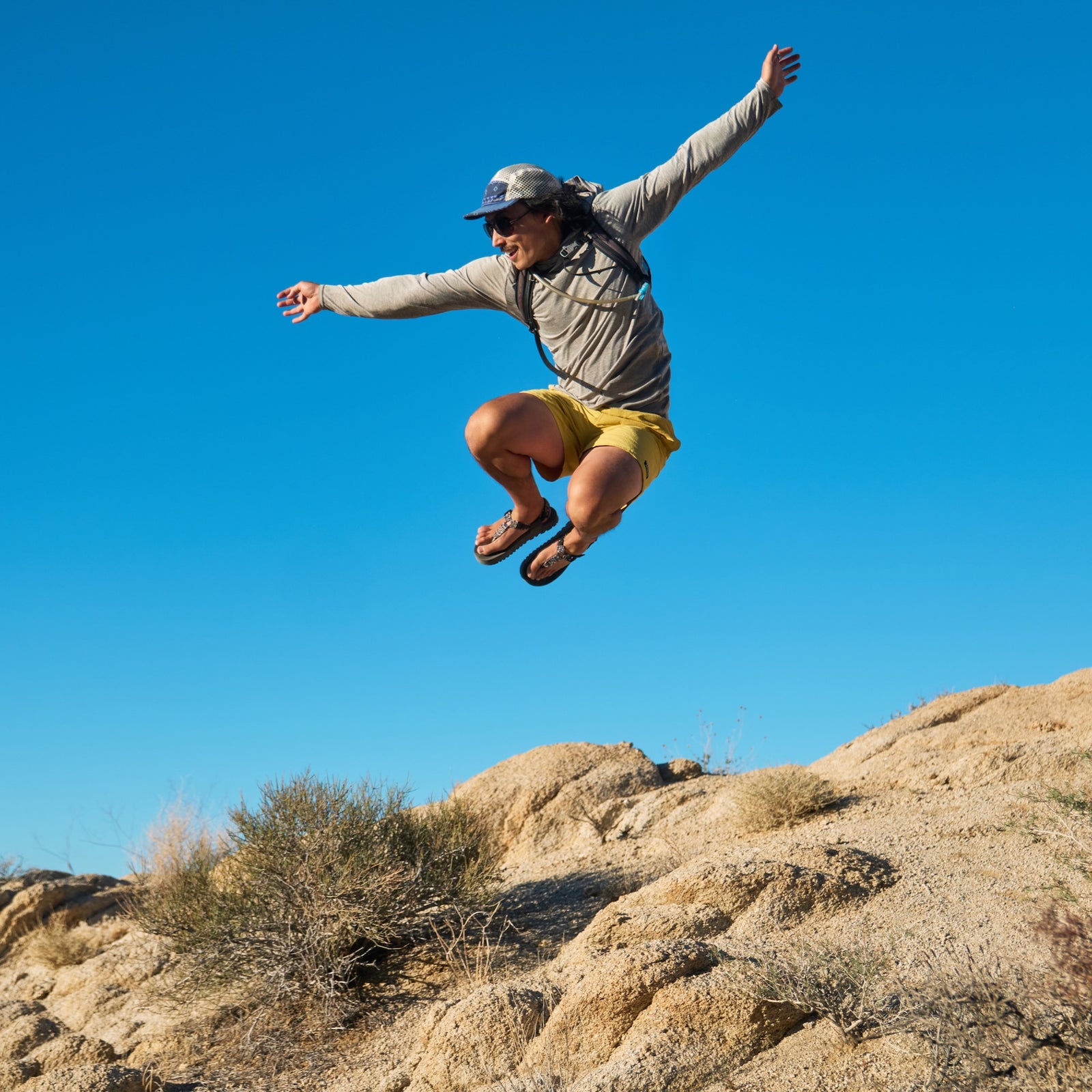 Person jumping in the air with a clear blue sky and desert landscape wearing Bedrock Cairn Sandals