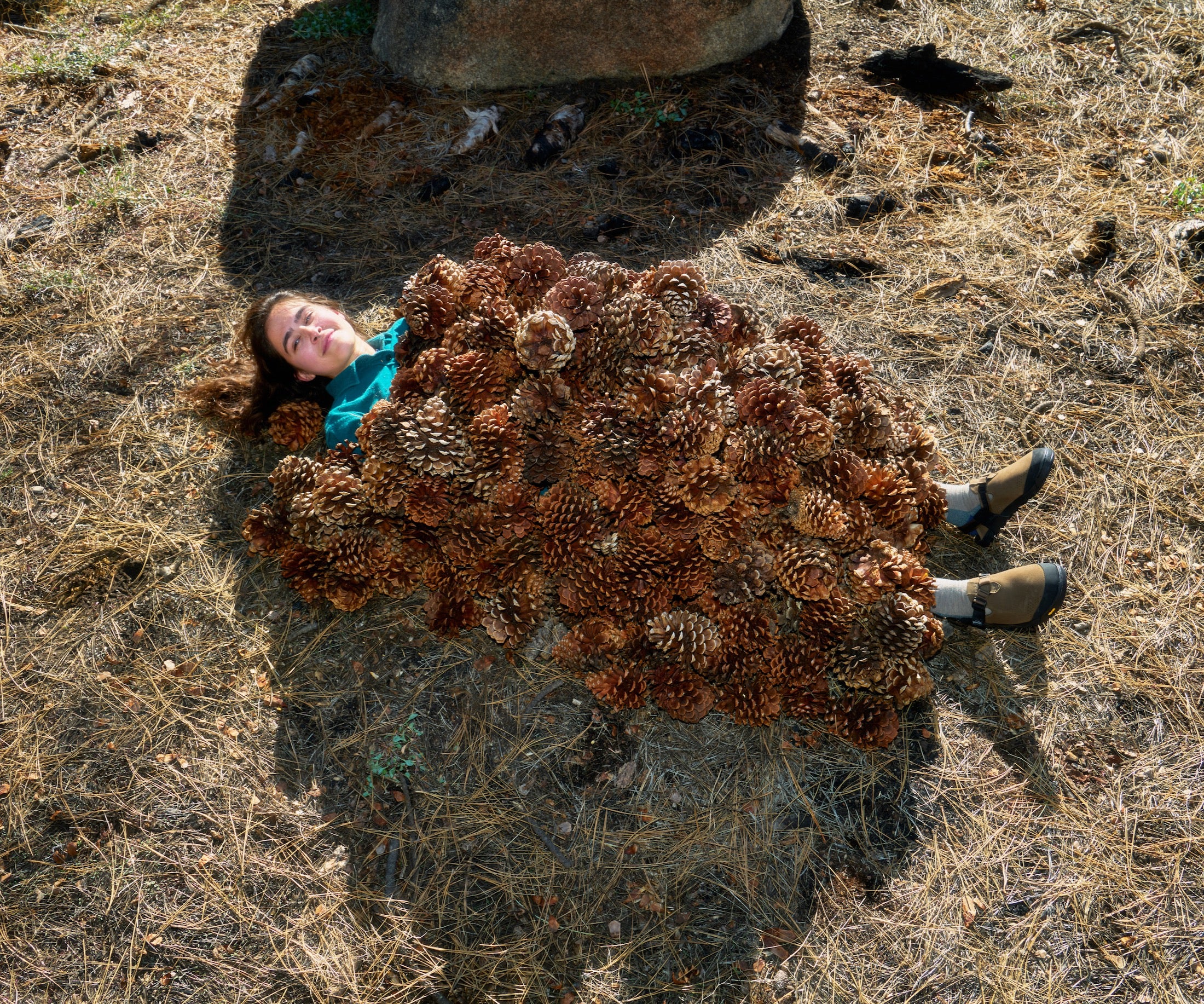 Person lying on a large cluster of brown pinecones in a natural setting wearing Pinecone Synthetic Suede Mountain Clogs 