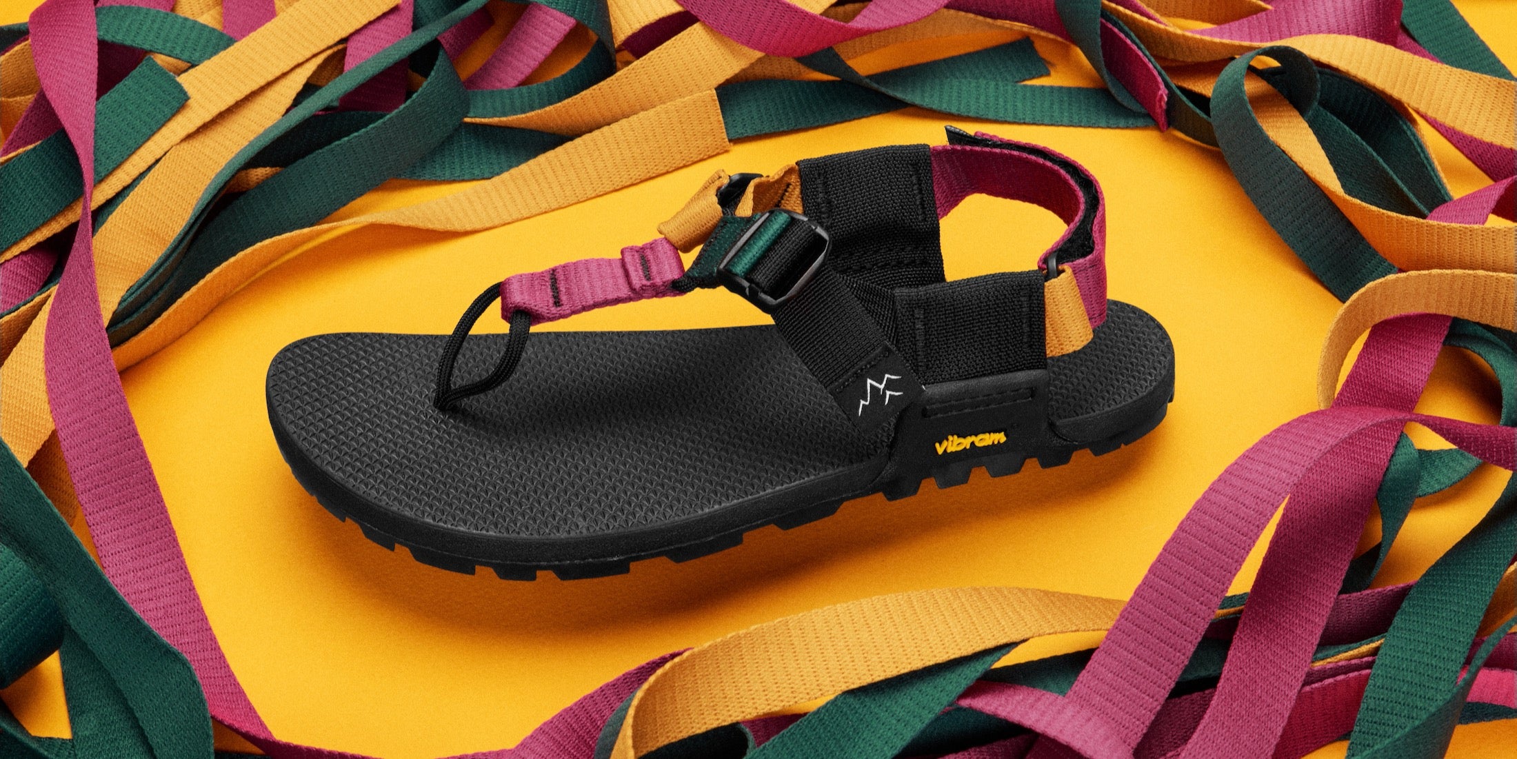Metamorphic tourmaline cairn sandals photgraphed in yellow background with webbing colors