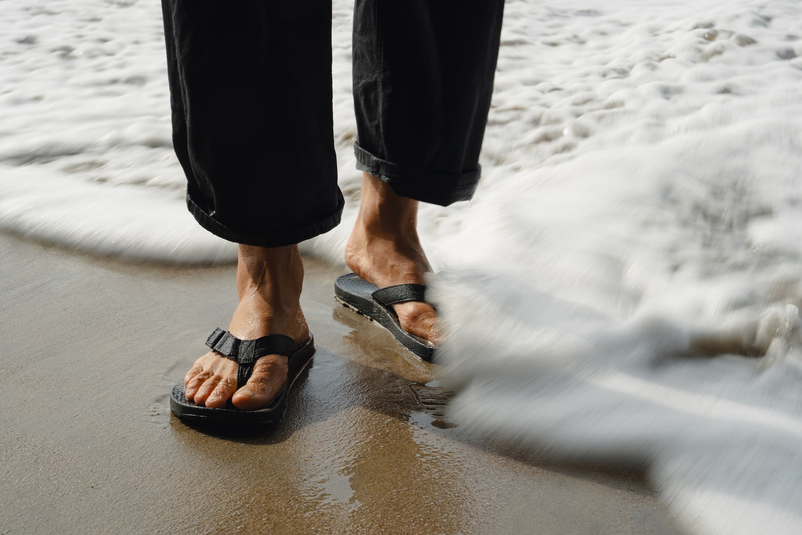 Person wearing black rockhound sandals standing on a beach with waves.