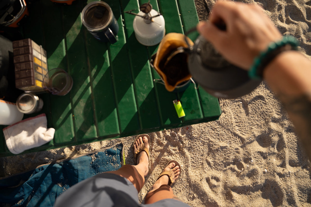 Person preparing a drink on a green folding table at the beach wearing nubuck leather rockhound sandals