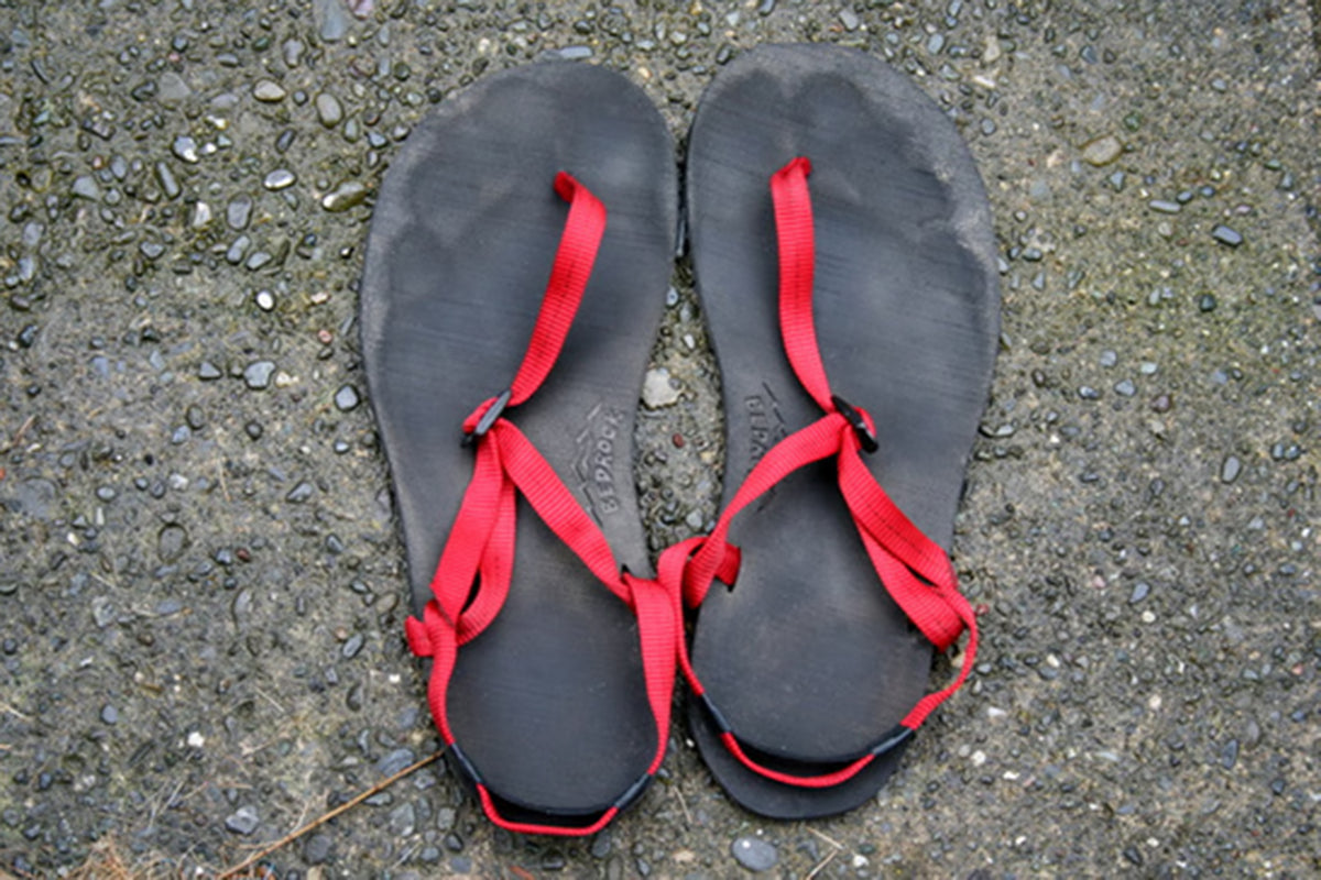 A pair of black flip-flop sandals with bright red straps laid flat on a textured gray asphalt surface.