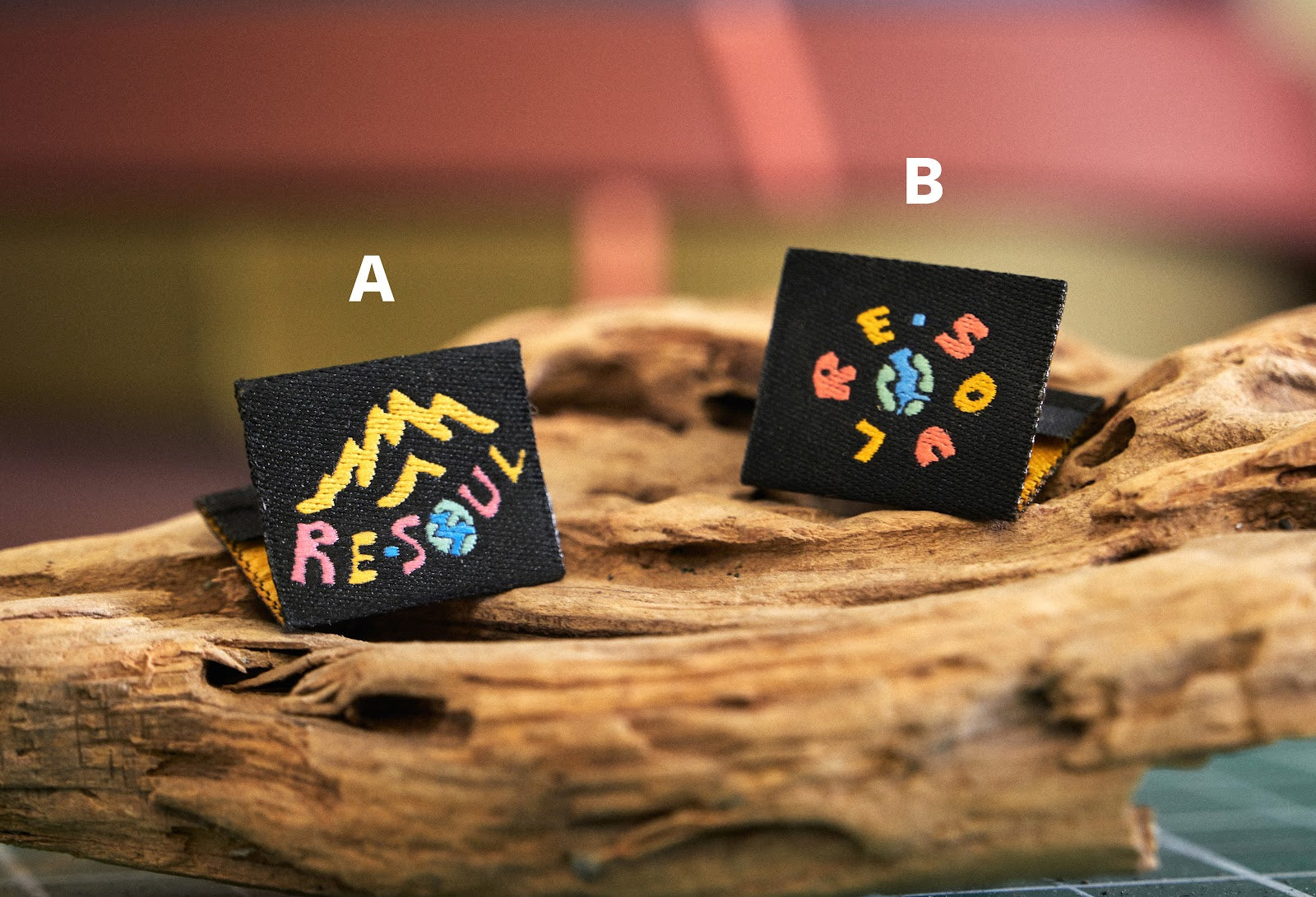 Two embroidered patches labeled A and B on a wooden surface with a blurred background